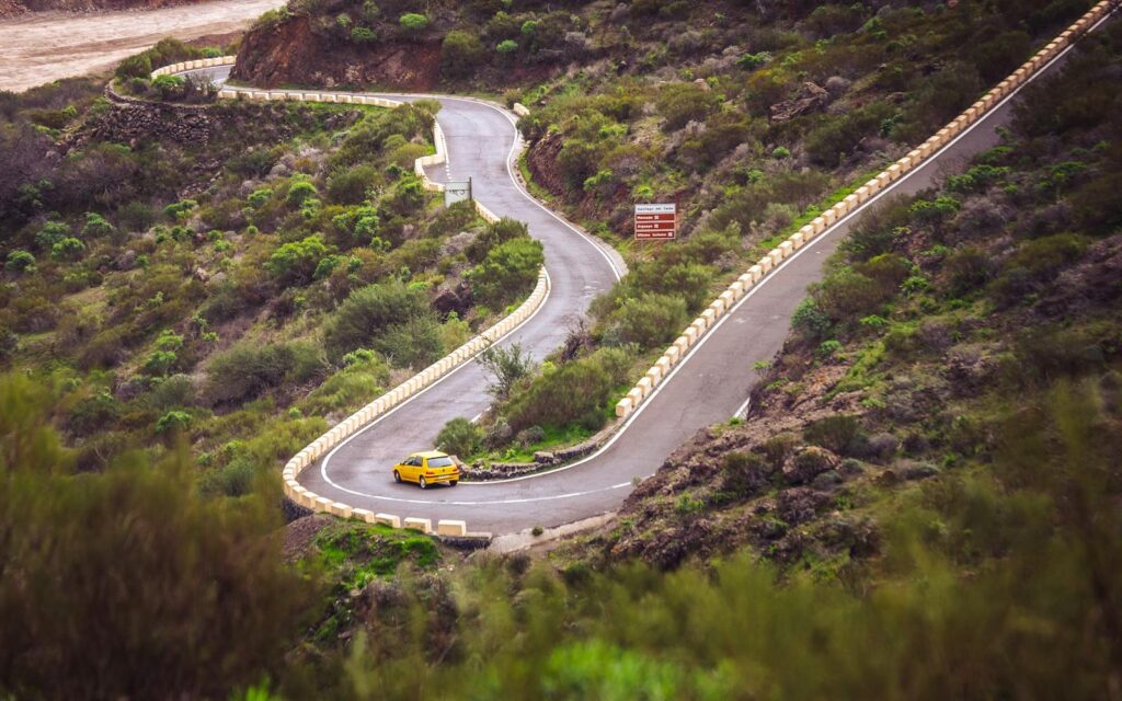 A yellow car navigates a winding mountain road in Santa Cruz de Tenerife, Spain.
