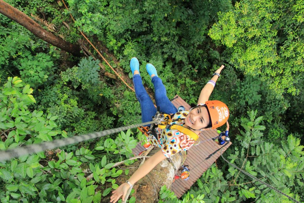 Woman enjoying a thrilling zipline experience in Phuket, Thailand's vibrant green forest.